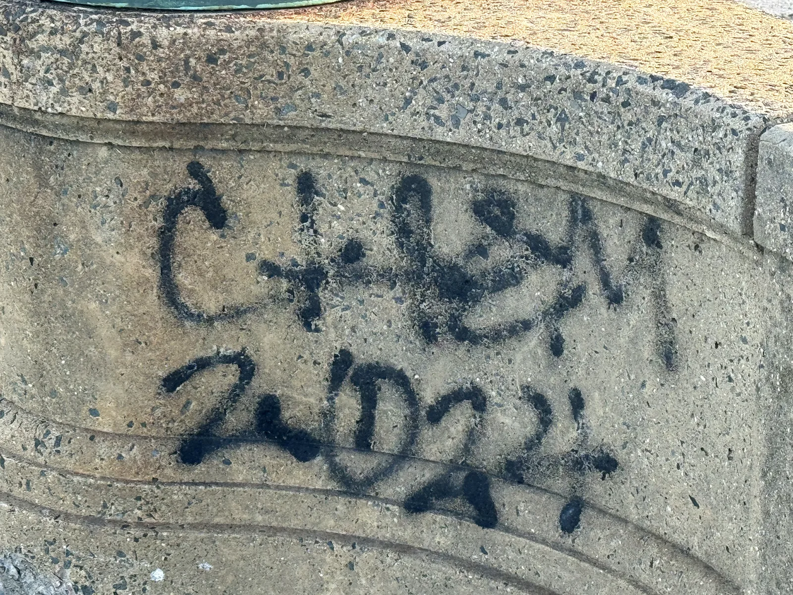 Black spray-painted tag scrawled on a granite pier of the bridge